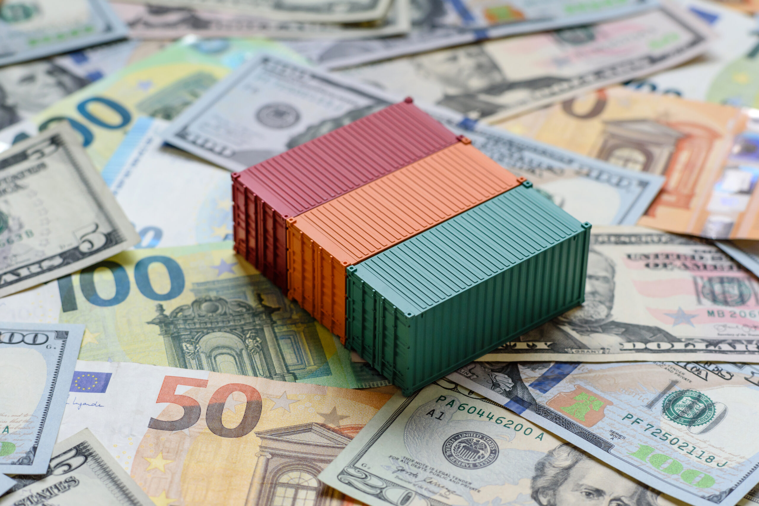 Contêineres sobre cédulas de dólar e euro representam o drawback suspensão, a importação de insumos, a suspensão de tributos e a gestão de custos no comércio exterior.