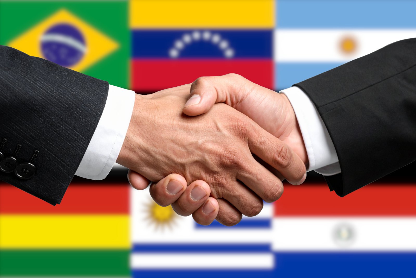 Bandeiras dos países do Mercosul e aperto de mãos, símbolo de acordo comercial.